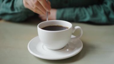 Beyaz bir fincanda bir fincan aromatik koyu kahveyi karıştıran bir kadının el resmi. Huzurlu bir kahve molasının özünü mükemmel bir şekilde yakalıyor.