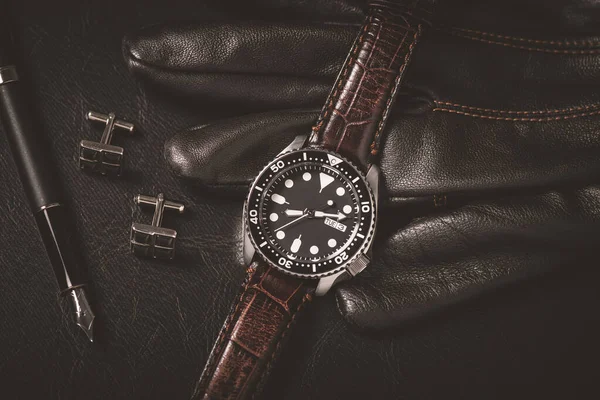 Men accessories on black leather. Closeup at luxury men watch with black dial and leather strap.