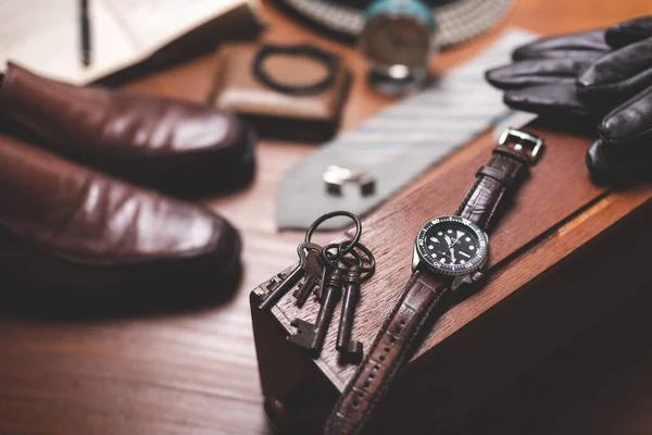 Men accessories on wooden desk. Closeup at luxury men watch with black dial and leather strap.