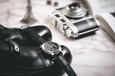 Men accessories on white marble background. Closeup at luxury men watch with black dial and leather strap.