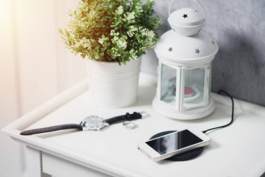 Akıllı telefonu beyaz masada kablosuz şarj cihazıyla şarj etmek..