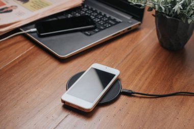 Akıllı telefonu ahşap masada kablosuz şarj cihazıyla şarj etmek..