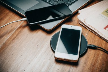Akıllı telefonu ahşap masada kablosuz şarj cihazıyla şarj etmek..