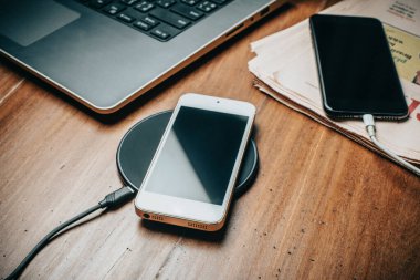 Akıllı telefonu ahşap masada kablosuz şarj cihazıyla şarj etmek..