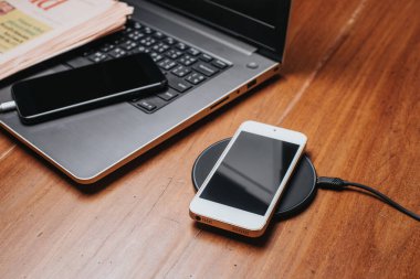 Akıllı telefonu ahşap masada kablosuz şarj cihazıyla şarj etmek..