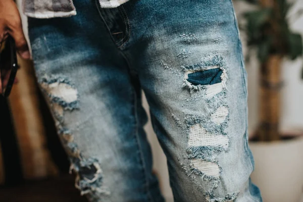 The man wearing distressed jeans. Fashion blue denim jeans. Closeup at ripped on jeans.