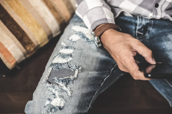 The man wearing distressed jeans. Fashion blue denim jeans. Closeup at ripped on jeans.