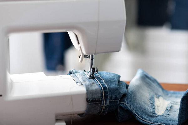 Портной работает с джинсами в синих джинсах. Портной подогнал джинсы..