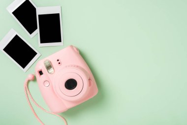 Yeşil zemin üzerinde boş anlık filmler olan pembe fotoğraf makinesi..