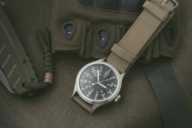 Biege naylon saat bandıyla askeri kol saatini kapat. Arka planda askeri nesneler olan erkekler için kol saati.