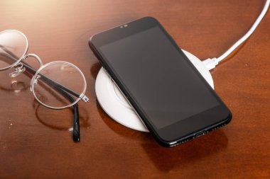 Akıllı telefonu ahşap masadaki kablosuz şarjla şarj etmek. Modern yaşam tarzı kavramı.
