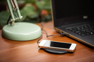Akıllı telefonu ahşap masadaki kablosuz şarjla şarj etmek. Modern yaşam tarzı kavramı.