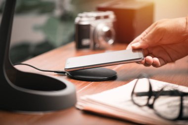 Akıllı telefonu ahşap masadaki kablosuz şarjla şarj etmek. Modern yaşam tarzı kavramı.