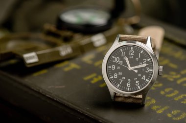 Biege naylon saat bandıyla askeri kol saatini kapat. Arka planda askeri nesneler olan erkekler için kol saati.