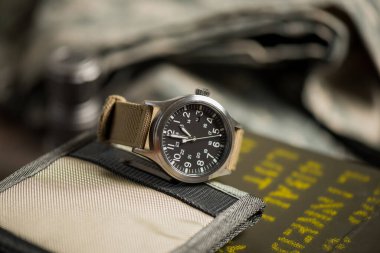 Biege naylon saat bandıyla askeri kol saatini kapat. Arka planda askeri nesneler olan erkekler için kol saati.