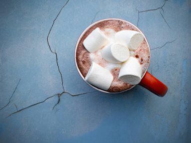 Eski püskü mavi bir yüzey üzerinde lokum kaplı bir fincan sıcak çikolata..