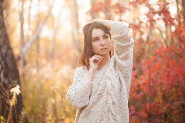 Güz ormanında poz veren beyaz kazaklı güzel bir kadın.