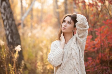 Güz ormanında duran beyaz kazaklı güzel bir kadın.