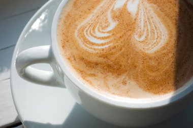 Beyaz bardakta tarçınlı kapuçino. Kapat.