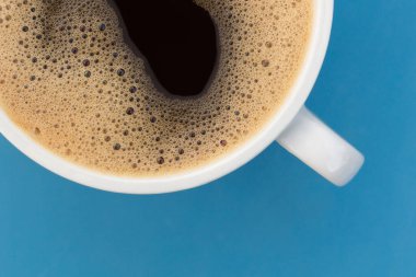 Mavi bir yüzey üzerinde beyaz bir fincanda köpüklü sade kahve. Kapat şunu.