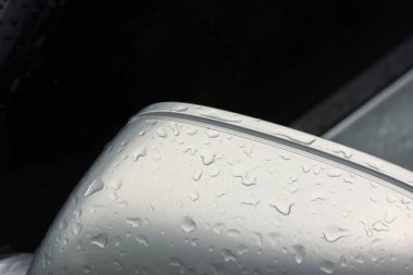 Yağmur damlalarıyla kaplı bir arabanın yan aynası. Kapat.