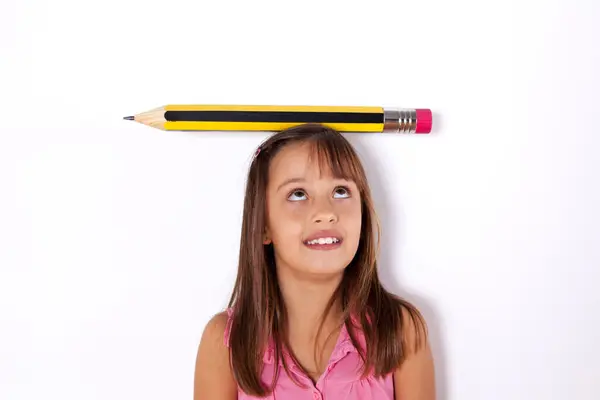 彼女の頭の上に巨大な鉛筆で壁の隣に小さな女の子 — ストック写真