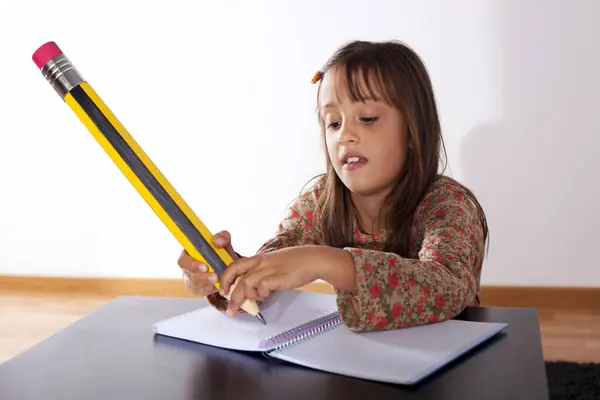 小女孩在家里用一支巨大的铅笔写字 图库照片
