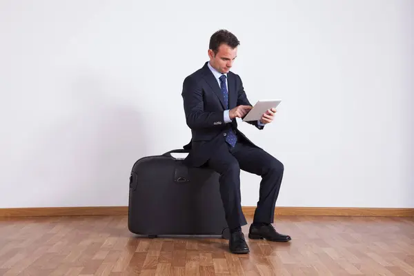 ビジネスマンはデジタルタブレットを使用して旅行の荷物に座ります ロイヤリティフリーのストック画像