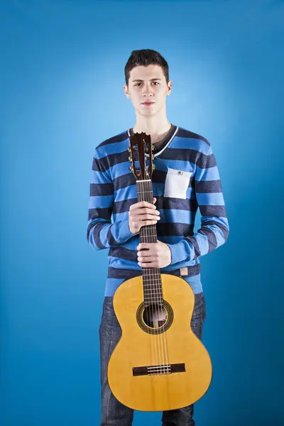 Teenager holding a classic guitar with blue background