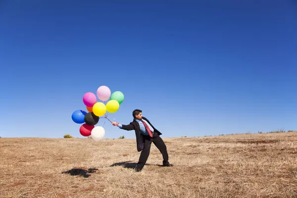 Businessman at the field holding colorful balloons
