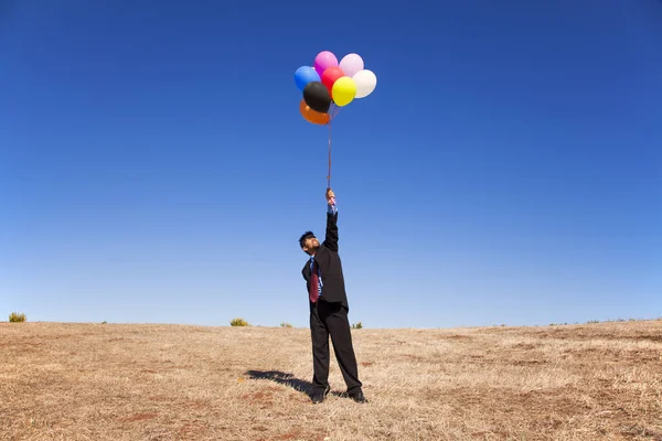 Businessman at the field holding colorful balloons