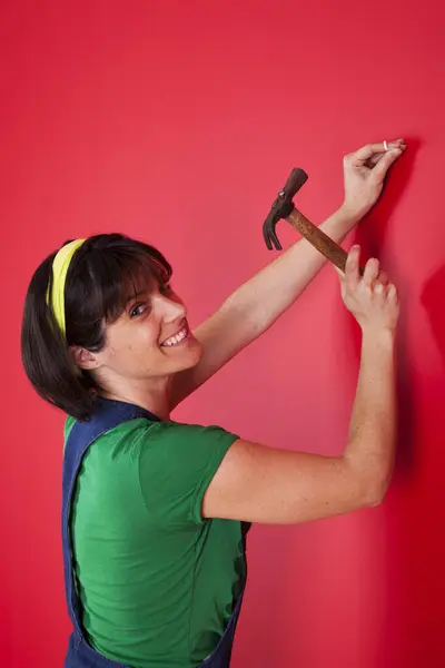 woman driving a nail in a red wall
