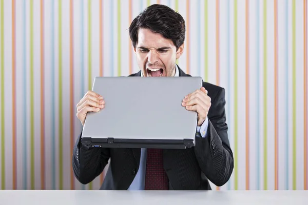 彼のノートパソコンを食べている狂ったビジネスマン ストック画像