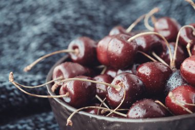 Koyu mavi örülü bir battaniye üzerinde olgun kırmızı kirazlarla dolu bir kase..