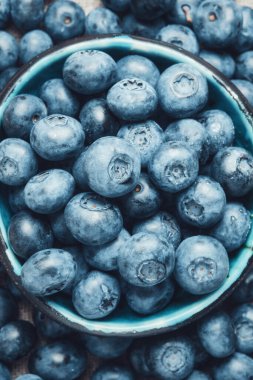Blueberries in a ceramic bowl and lots of berries around. Blue background.