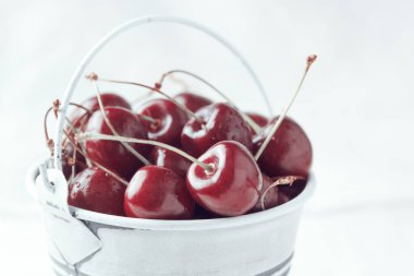 Arka planda kırmızı kiraz dolu küçük beyaz bir kova. Yakın plan. Parlak güneş ışığı.