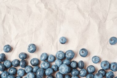 Fresh blueberries scattered on beige craft paper.