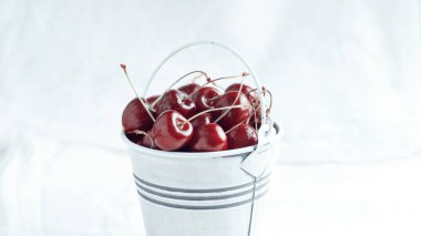 Small white bucket full of red cherries on a light background. Bright sunlight.