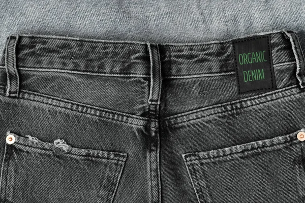 Black jeans labeled ORGANIC DENIM. Sustainable fashion, conscious consumption, trendy clothing.