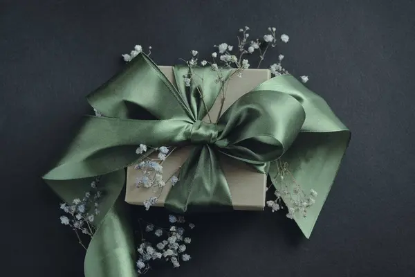 小さな花 黒い背景に結ばれたオリーブの緑のリボンが付いている紙のギフト用の箱 誕生日 結婚式のための装飾 — ストック写真
