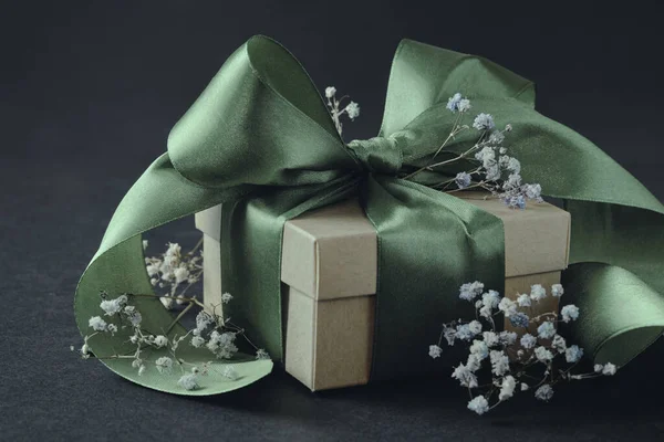 小さな花 黒い背景に結ばれたオリーブの緑のリボンが付いている紙のギフト用の箱 誕生日 結婚式のための装飾 — ストック写真