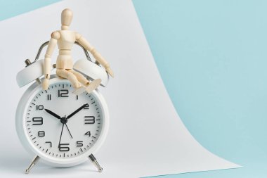 Tahta bir adam beyaz bir çalar saatin üzerinde oturur. Zaman yönetimi, zaman kontrolü, dakiklik.