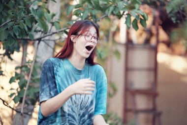 Şaşırmış kırmızı saçlı genç kız mavi tişörtlü gözlüklü..