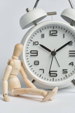 Tahta adam beyaz bir çalar saatin yanında oturuyor. Geç kalma kavramı, uzun bekleyiş, zamanın geçişi, yaşlılık..