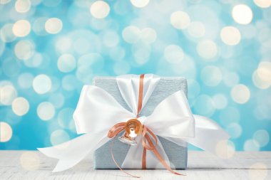 Mavi gümüş kağıda sarılı, beyaz ve altın kurdeleli hediye kutusu. Mavi arka plan, bokeh ışığı. Noel ve Yeni Yıl Hediyeleri, Boks Günü.