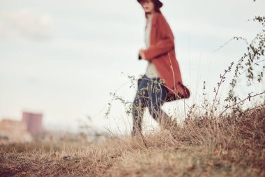 Ön planda kuru sonbahar otları, gökyüzü ve arka planda kırmızı bir ceket ve şapkayla koşan bulanık bir kız.