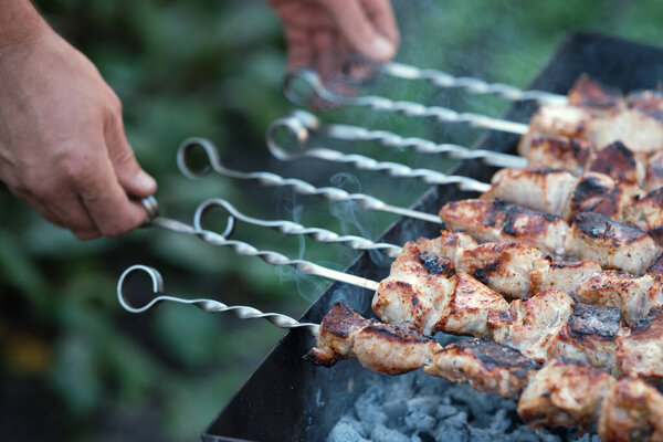 Cooking pork barbecue. Male hands turns skewers with meat.