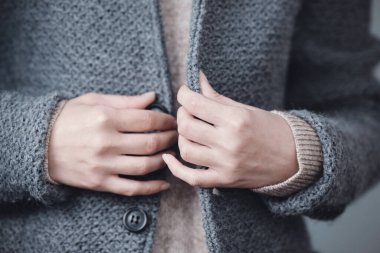 Gri örgü bir ceketin yakın çekimi. Kadın elleri düğmeleri bağlar. Kış, sonbahar sıcak yün giysiler.