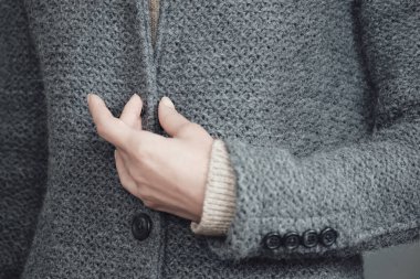 Gri örgü bir ceket ve bir kadının elinin yakın çekimi. Kış, sonbahar sıcak yün giysiler.