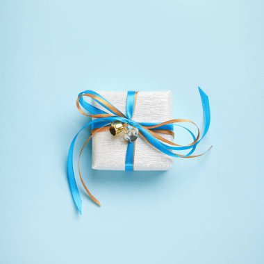 Mavi ve altın kurdeleli gümüş kağıda sarılı hediye kutusu. Mavi arka plan, üst manzara. Noel ve Yeni Yıl Hediyeleri, Boks Günü.